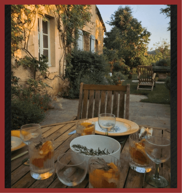 Outdoor dining setup with glasses of drinks and a bowl, in a garden setting at sunset.