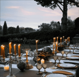 Outdoor dining table with candles, glassware, and elegant table settings at dusk.