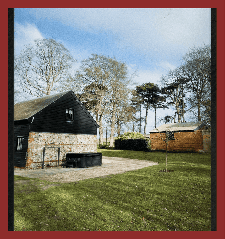 Charming rural house with black wood exterior, surrounded by lush green lawn and tall trees.