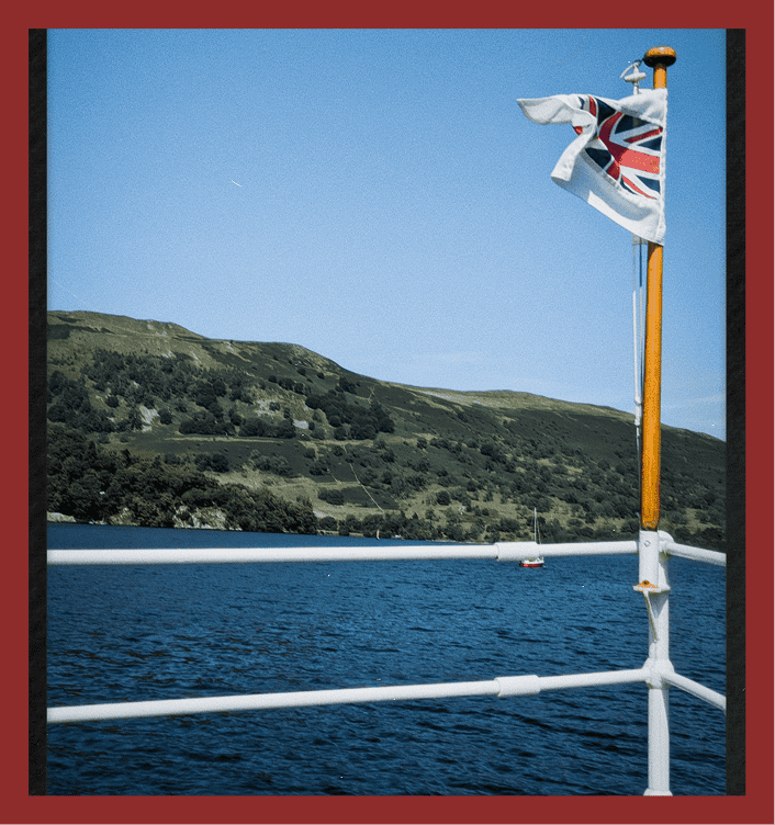 British Union Jack flag flying on a boat in a picturesque harbor setting.