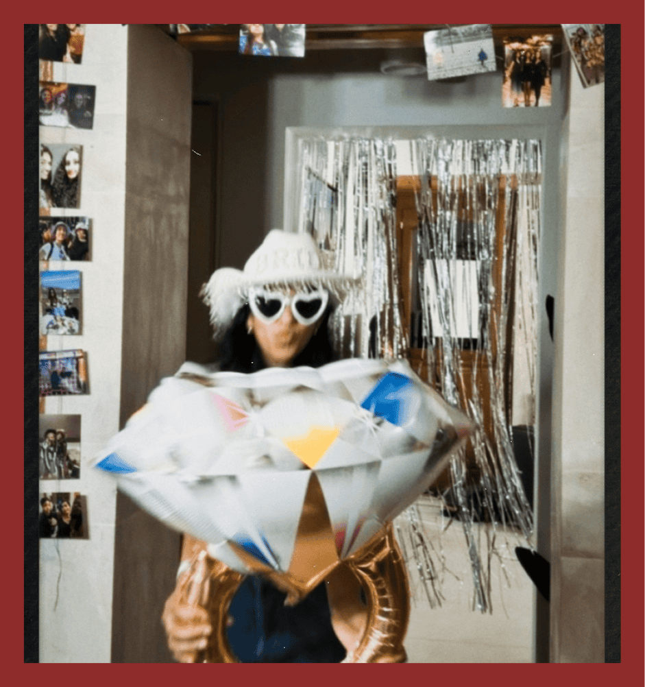 Woman holding colorful balloons, wearing heart-shaped sunglasses and a fluffy hat.