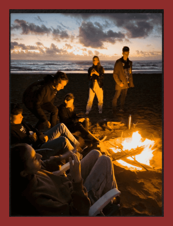 People enjoying a beach bonfire at sunset with friends, relaxing by the warm fire on the sandy shore.